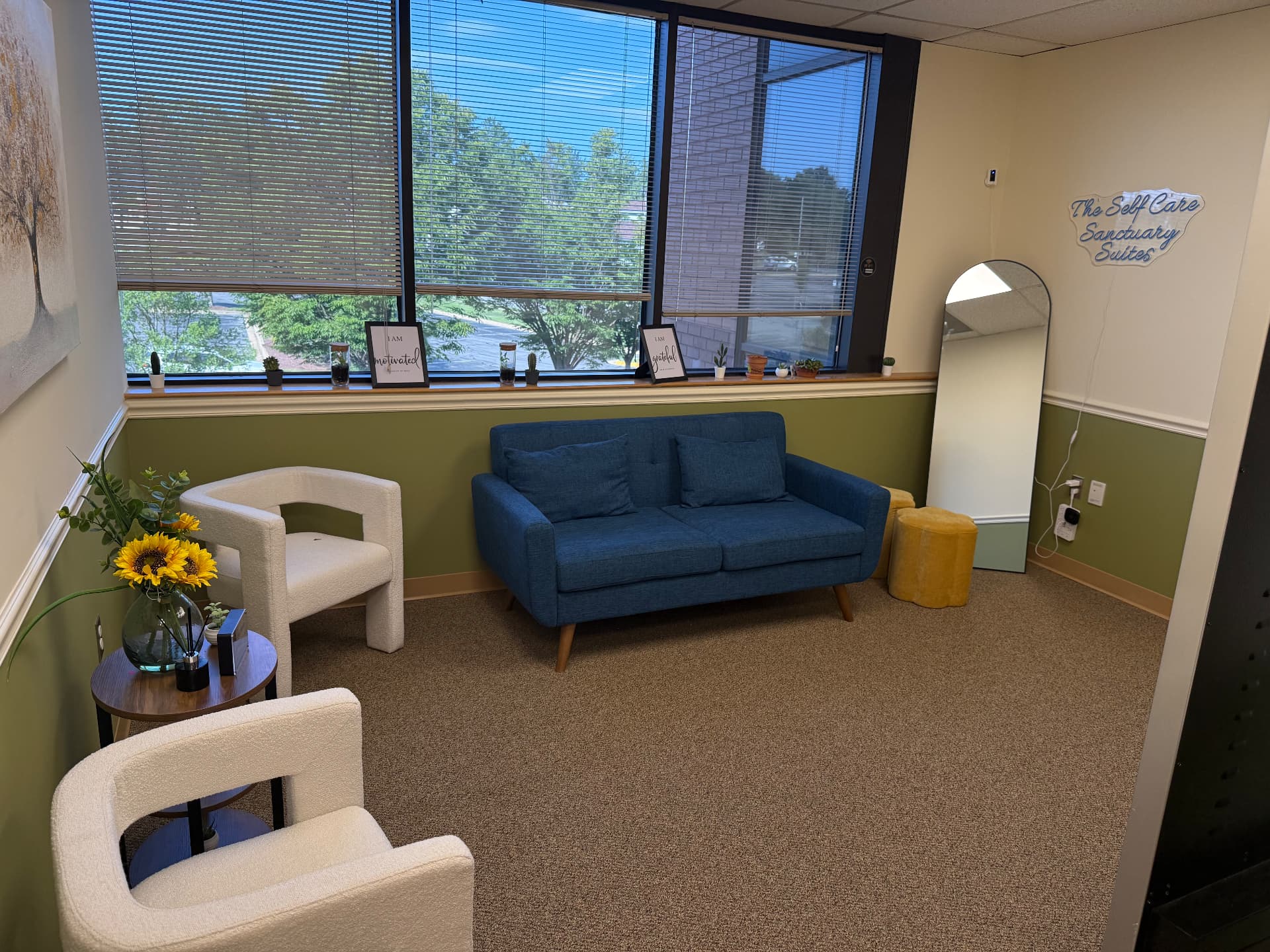 Welcoming lobby with a blue sofa, seating and a neon Self Care Sanctuary Suites sign at the entrance in Laurel, Maryland